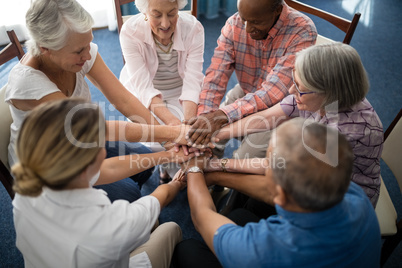 High angle view of female doctor amidst seniors stacking hands