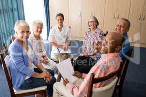 High angle portrait of smiling seniors and female doctor sitting on chairs