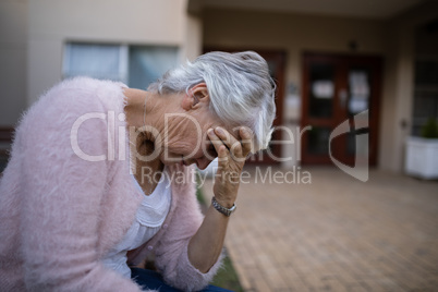 Side view of depressed senior woman sitting on bench with head in hand