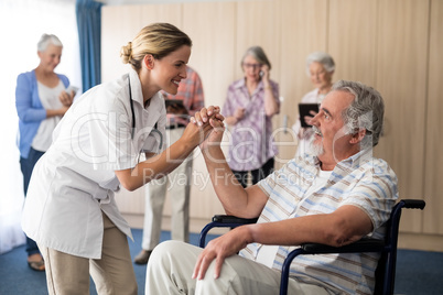 Smiling female doctor holding hands with disabled senior man sitting on wheelchair