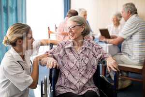 Cheerful disabled senior woman sitting on wheelchair looking at female doctor