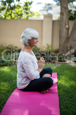 Side view of senior woman meditating on exercise mat