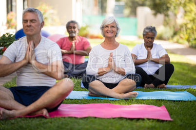 Smiling senior woman meditating in prayer position with friends