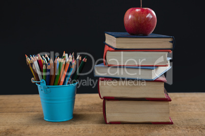 Apple on book stack with color pencils on table