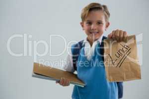 Smiling schoolboy holding book and lunch paper bag