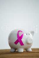 Pink Breast Cancer Awareness ribbon on piggybank over wooden table