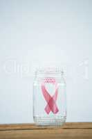 Pink Breast Cancer Awareness ribbon in glass jar on piggybank on wooden table