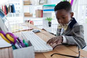 Boy imitating as businessman using computer at desk