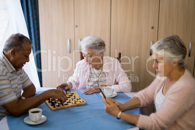 Senior friends playing chess and having coffee