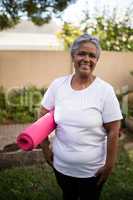 Smiling senior woman standing with exercise mat at park
