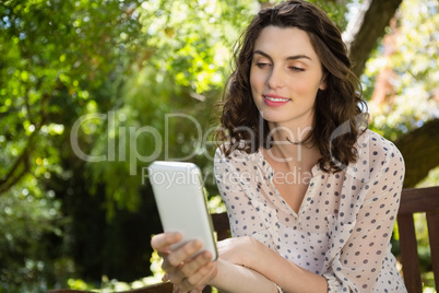 Woman sitting on bench and using digital tablet in garden on a sunny day