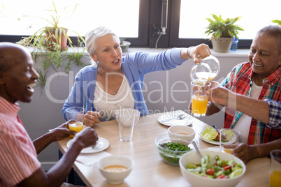 Senior woman talking while serving juice to friends