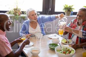 Senior woman talking while serving juice to friends