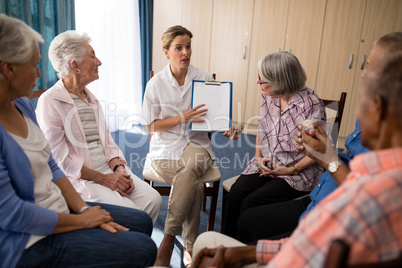 Female doctor explaining with clipboard to seniors sitting on chairs