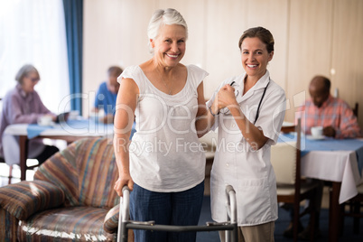 Portrait of smiling senior woman holding hands with female doctor by walker