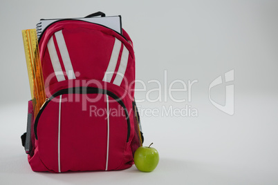 Schoolbag with various supplies and apple on white background