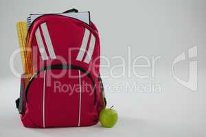 Schoolbag with various supplies and apple on white background