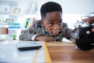 Bored businessman checking alarm clock while leaning on desk