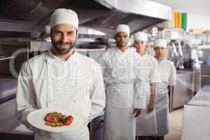 Smiling chef holding delicious dish in kitchen