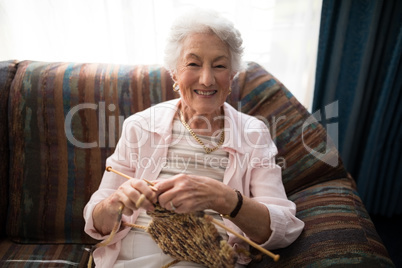 Portrait of smiling senior woman knitting while sitting on sofa against window