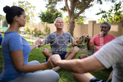 Trainer meditating with senior people while holding hands
