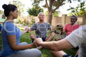 Trainer meditating with senior people while holding hands