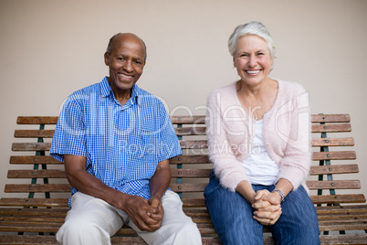 Portrait of smiling senior woman and man sitting on bench against wall