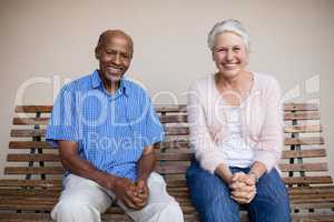 Portrait of smiling senior woman and man sitting on bench against wall