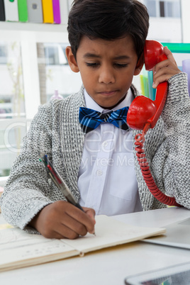 Boy imitating as businessman writing on book while using landline