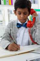 Boy imitating as businessman writing on book while using landline