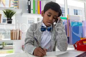 Businessman writing on book while talking on mobile phone