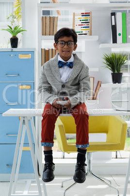 Full length portrait of businessman holding smart phone while sitting on desk
