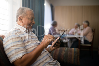 Happy senior man using phone while sitting on sofa