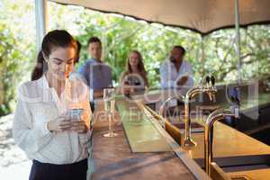 Smiling woman using mobile phone while having a glass of champagne