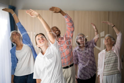 Smiling female doctor and seniors exercising with arms raised