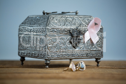 Surface level view of pink Breast Cancer Awareness ribbon with chest and rings on wooden table