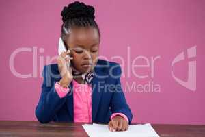 Businesswoman talking on mobile phone while reading documents