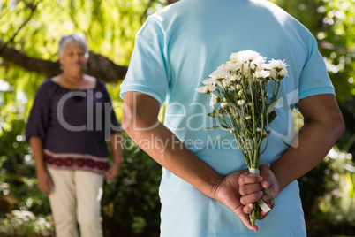 Mid-section of senior man hiding flowers behind back