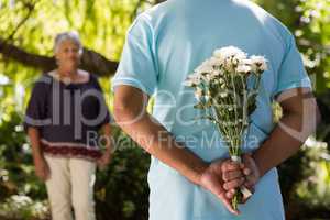 Mid-section of senior man hiding flowers behind back