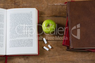 Opened book, green apple and chalk on wooden table