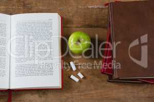 Opened book, green apple and chalk on wooden table