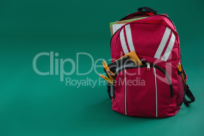 Schoolbag with various supplies on green background
