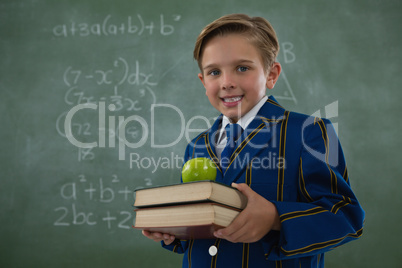 Schoolboy holding books stack with apple against chalkboard