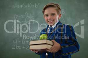 Schoolboy holding books stack with apple against chalkboard