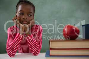 Schoolgirl sitting beside books stack against chalkboard