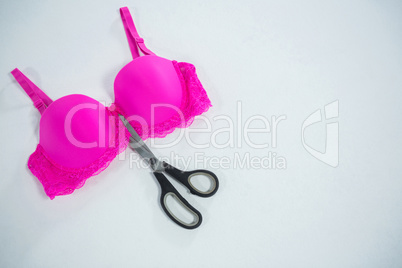 High angle view of vibrant pink bra with scissors