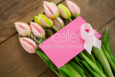High angle view of pink Breast Cancer Awareness ribbon with blank card on tulips