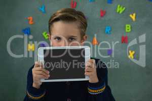 Schoolboy holding digital tablet against chalkboard