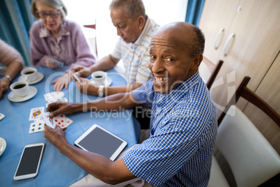Happy senior man playing cards with friends