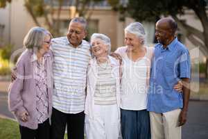 Smiling senior friends standing with arms around